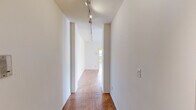 This 1-bedroom, 1-bathroom residence offers a thoughtfully organized single-floor layout that makes efficient use of its space. A defining characteristic throughout the home is the warm herringbone parquet wood flooring, which runs consistently across the living room, hallways, and bedroom, lending a timeless, classic aesthetic to the interior.

The spacious living room is bathed in natural light through large windows that offer views of the surrounding neighborhood and skyline. A ceiling fan overhead adds both comfort and a clean, functional touch. The room's neutral white walls and open layout create a versatile and airy atmosphere.

The kitchen features white cabinetry extending to the ceiling for ample storage, a white countertop, a gas range, a dishwasher, and a sink positioned near a window — keeping the space bright and practical. The floor transitions to a light tile, distinguishing it from the rest of the home.

The bedroom is a well-proportioned retreat with its own ceiling fan, herringbone parquet flooring, and a window that frames rooftop and neighborhood views, complemented by a baseboard heating unit.

The bathroom is finished with warm yellow wall tiles, a mosaic tile floor, an oval mirror, wall sconce lighting, and a combined tub and shower. Two hallways connect the rooms fluidly, with track lighting guiding the way through the home.