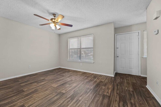 Habitación vacía con suelo de vinilo imitación madera oscura, ventilador de techo con luz, ventana con persianas y puerta de armario blanca. - Walnut Creek at 122