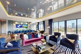Located at 501 NW Seventh Ave in Fort Lauderdale, FL, this upscale amenity lounge delivers a striking blend of contemporary design and resort-style comfort across a generously proportioned single floor. The interior is immediately distinguished by its dramatic high-gloss reflective ceiling framed with gold-lit cove lighting, creating a luminous, jewel-box ambiance throughout the main lounge. Floor-to-ceiling glass walls and sliding doors flood the space with abundant natural light while framing panoramic views of the Fort Lauderdale skyline and surrounding cityscape.

The main lounge area features bold, curated furnishings including a vibrant magenta velvet sofa, deep navy accent chairs, and a graphic black-and-white zebra-print area rug layered over an intricate parquet hardwood floor. A dedicated bar and social zone at the rear showcases a sleek counter lined with cobalt blue barstools, globe pendant lighting, a tiled accent wall, and a wall-mounted display screen — ideal for gatherings and events.

The space seamlessly transitions to two distinct outdoor terraces. One features a pergola-covered lounge with plush sectional seating and commanding skyline views, while the other offers alfresco dining tables bathed in South Florida sunshine. Together, these areas create a well-rounded environment suited for both relaxed socializing and curated events.