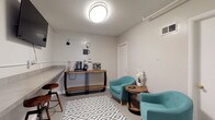 Located at 884 Thurber Dr W in Columbus, Ohio, this single-floor amenity space is designed to serve residents with functional, well-appointed communal facilities. The entrance welcomes visitors through a glass-paneled door with a slim hairpin-leg console table, offering a clean and minimal first impression with easy access to the interior.

The central lounge and common area is finished in neutral tones with large-format tile flooring and features a geometric-patterned area rug that anchors a seating arrangement of teal upholstered chairs and a round wood side table. A built-in countertop with bar-height stools lines one wall, providing a practical workspace, while a dedicated coffee and beverage station sits nearby on a rustic wood-and-metal console, complete with a Keurig machine and supplies. The space is well-lit with flush-mount ceiling fixtures throughout.

Adjacent to the lounge is a fully equipped laundry room, distinguished by its bold teal accent walls and concrete flooring. Multiple front-loading washers and dryers line both sides of the room, with a butcher-block folding table centered in the space for convenience. The layout is efficient and practical, making laundry tasks straightforward. Together, these spaces form a cohesive and thoughtfully designed amenity level suited for everyday residential use.