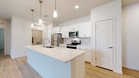 Located at 2121 N 99th Ave in Phoenix, AZ, this well-appointed single-story home offers three bedrooms and two full bathrooms within a thoughtfully designed open floor plan. The heart of the home is a contemporary kitchen that flows seamlessly into the living room, anchored by a generous island with a quartz countertop, an undermount sink, and stylish pendant lighting. White shaker cabinetry, a subway tile backsplash, and a full suite of stainless steel appliances — including a refrigerator, range, microwave, and dishwasher — complete the kitchen's clean, modern aesthetic. Light wood-look flooring extends throughout the entire home, creating a warm and cohesive feel. The living area is bright and open, with a ceiling fan, a sliding glass door providing access to an outdoor space, and natural light from windows dressed with blinds. The spacious primary bedroom features its own walk-in closet with built-in shelving and hanging rods. Secondary bedrooms each include ceiling fans, natural light, and closet space — one with sliding panel doors. Both bathrooms are finished with white vanities, quartz countertops, and tub-shower combinations with subway tile surrounds. A dedicated laundry room houses a full-size washer and dryer, rounding out the functional layout of this move-in-ready Phoenix home.