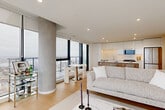 Located in Halifax, NS, this contemporary high-rise unit offers a thoughtfully designed open-concept layout finished with light hardwood flooring and recessed lighting throughout. The combined kitchen and living area serves as the heart of the home, anchored by a striking waterfall-edge marble island that provides generous prep and dining space. The kitchen features sleek white cabinetry extending to the ceiling, stainless steel appliances, and a clean, minimalist aesthetic. The living room is bathed in natural light through dramatic floor-to-ceiling windows framed by a signature exposed concrete column, offering panoramic views of the Halifax skyline and harbour. A private balcony extends the living space outdoors, delivering breathtaking elevated views of the city and waterfront. The spacious primary bedroom continues the floor-to-ceiling window theme, filling the room with light and cityscape vistas, while maintaining a calm, restful atmosphere. The bathroom is finished with large-format stone-effect tiles, a frameless glass sliding shower enclosure, and a white floating vanity. Well-proportioned hallways connect each space with ease, and a dedicated closet provides practical storage. The overall ambiance is modern, bright, and refined.