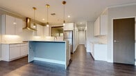 19 North is a thoughtfully designed single-floor residence that blends contemporary aesthetics with high-end finishes throughout. The open-concept kitchen serves as the heart of the space, showcasing a striking central island with granite countertops and a light blue base, complemented by crisp white cabinetry that extends to the ceiling. Gold-brushed pendant lights hang above the island, adding warmth to the clean, modern palette. Stainless steel appliances, including a professional-grade gas range with a stainless hood, and a built-in refrigerator, complete the chef-inspired kitchen. Dark hardwood flooring runs consistently throughout the living areas and bedrooms, grounding the light-toned walls and creating a cohesive, refined atmosphere. The bedrooms are generously proportioned, featuring neutral walls, clean white trim, and large black-framed windows that invite natural light and offer views of the surrounding streetscape. The bathroom is a standout feature, finished with floor-to-ceiling marble-style tile, a frameless glass walk-in shower, hexagonal floor tiles, and a wood-toned vanity with open shelving and a backlit mirror. Every detail of this residence reflects a commitment to modern design and quality craftsmanship.