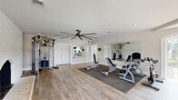Located at 1230 Cottontown Rd in Forest, VA, this dedicated fitness facility offers a thoughtfully designed single-floor layout spanning a generously sized footprint. The space is divided into two distinct exercise rooms, each tailored to different training modalities, supported by a full bathroom and a closet for added convenience.

The main exercise room features light hardwood-style flooring, neutral gray walls, and large wall-mounted mirrors that amplify the sense of space. A large-blade ceiling fan provides airflow overhead, while recessed lighting ensures a bright, clean environment. This room is equipped with strength machines, adjustable benches, dumbbells, a cable system, and a spin bike, making it versatile for a wide range of workouts.

A standout second exercise room boasts a striking white brick fireplace as a central architectural feature, arched windows that flood the space with natural light and outdoor views, and high ceilings with an oversized ceiling fan. Treadmills, ellipticals, and a wall-mounted TV make this an ideal cardio zone. A third area serves as a dedicated boxing and functional training room, featuring a heavy bag, floor-to-ceiling mirror, and large windows overlooking the outdoors.

The bathroom is finished with tile flooring, white cabinetry, a marble-top vanity, and a framed mirror with vanity lighting, providing a clean and functional post-workout retreat.