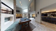 This expansive amenity lounge is designed to impress, combining contemporary architecture with thoughtfully curated entertainment and social spaces. Soaring double-height ceilings flood the main area with natural light through floor-to-ceiling glass doors that open to an outdoor patio beyond. A dramatic stacked-stone accent wall anchors the lounge seating area, which features an inset fireplace and a wall-mounted television, surrounded by plush cream armchairs and rich dark wood furnishings that create an inviting atmosphere.

The games area is a standout highlight, housing a classic billiards table on stone-look tile flooring alongside a shuffleboard table set against a bold teal accent wall with its own dedicated seating nook and mounted display screen. Pendant globe lighting and wall sconces add warm, layered illumination throughout.

A sophisticated full-service bar area offers bar-height seating along a sleek counter, pendant lighting above a stone-tile backsplash, and an integrated television — ideal for social gatherings. A compact wet bar with a draft tap and a cozy banquette booth with a marble-top table provide additional intimate entertaining options. Neutral stone-look tile flooring, curated artwork, and a consistent palette of warm grays, browns, and teal accents tie all zones together into a cohesive, upscale communal retreat.