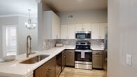 This single-story home showcases a thoughtfully designed interior with a cohesive, modern aesthetic throughout. The main living area features warm hardwood-style flooring, neutral gray-toned walls, crown molding, and a ceiling fan with a brushed gold finish. Large windows fitted with white horizontal blinds allow generous natural light to fill the space, while an open passageway connects seamlessly to additional rooms.

The dining area is highlighted by a striking bay window arrangement and an elegant multi-light chandelier, creating a bright and inviting atmosphere with outdoor views of surrounding greenery.

The kitchen is a standout feature, boasting a two-tone cabinet design with crisp white upper cabinets and gray lower cabinets, white quartz countertops, a decorative Moroccan-style tile backsplash, stainless steel appliances, and a deep undermount sink. The layout provides ample workspace and storage.

Bedrooms continue the hardwood-style flooring and neutral palette, each with ceiling fans and natural light from well-placed windows. The primary bathroom offers a dual-sink vanity with dark cabinetry, white countertops, and framed mirrors. A spacious walk-in closet with built-in shelving and hanging rods provides excellent storage.

Additional conveniences include a dedicated in-unit laundry area with a full-size washer and dryer.