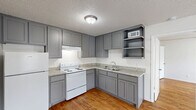 Located at 2413 W Prairie St in Denton, TX, this one-bedroom, one-bathroom unit offers a practical and efficiently designed single-floor layout. The kitchen is a standout feature, showcasing gray shaker-style cabinetry that extends to the ceiling, providing ample upper and lower storage. Open shelving adds additional display space, while granite-style countertops offer a clean, modern work surface. White appliances, including a refrigerator and electric range with overhead ventilation, complete the kitchen setup. Warm hardwood-style flooring runs throughout the unit, lending a cohesive and inviting feel to the space. The bedroom is a comfortable size, featuring a window with blinds that brings in natural light and offers exterior views. A dedicated closet with shelving and a hanging rod provides convenient storage directly off the bedroom. The bathroom includes a full tub-shower combination with clean, white surround walls and chrome fixtures. Textured ceilings are consistent throughout the unit, and flush-mount light fixtures provide ambient lighting in each room. The overall layout is straightforward and functional, making efficient use of the available space. This unit is well-suited for a single occupant seeking a manageable, move-in ready home in Denton.
