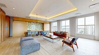 Located at 695 Atlantic St in Stamford, Connecticut, this thoughtfully designed communal lounge space offers a refined blend of modern aesthetics and functional versatility. The open single-floor layout is anchored by a striking tray ceiling with warm indirect cove lighting, creating an inviting and sophisticated ambiance throughout.

Light-toned hardwood-style flooring runs seamlessly across the space, complementing the bright, airy atmosphere generated by a generous array of oversized windows that frame sweeping views of the Stamford skyline. Sheer floor-length drapes soften the natural light while maintaining an open, connected feel with the outdoors.

The lounge area is thoughtfully furnished with a mix of comfortable sofas, mid-century modern accent chairs, and a wood-topped coffee table arranged atop a neutral area rug. A wall-mounted flat-screen TV sits above a sleek linear fireplace, adding both warmth and a focal point to the seating zone. Direct access to an outdoor terrace further extends the usable living space.

A dedicated dining area features a long communal table paired with light blue chairs, set against a warm wood-paneled wall adorned with a colorful mosaic tile accent and pendant lighting. A striking vertical wood slat partition elegantly divides zones within the space, adding architectural texture and visual depth. This well-appointed lounge is ideal for both relaxed gatherings and social events.