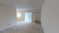 This single-floor unit offers a straightforward, functional layout designed to maximize usable living space. The open living and dining area is generously sized, finished with neutral-toned carpet throughout and bright white walls that create a clean, airy atmosphere. A large sliding glass door fitted with vertical blinds allows abundant natural light to flow into the main living space, while a secondary window further enhances the brightness of the area. A dedicated entry door provides a tiled foyer transition into the carpeted living zone, complete with a built-in closet for storage.

The kitchen is efficiently arranged and features light wood cabinetry providing ample upper and lower storage, a tile floor, a double-basin sink, a dishwasher, a coil-top electric range, and a refrigerator. Under-cabinet lighting illuminates the work surfaces, making the kitchen both practical and well-lit.

The bedroom is a comfortably sized, carpeted room with a window dressed with horizontal blinds, offering natural light and views to the exterior. The full bathroom includes a clean white soaking tub with a full surround, a toilet, and a vanity, all finished in neutral tones. Throughout the unit, the neutral color palette and open design provide a versatile canvas well-suited to a variety of uses.