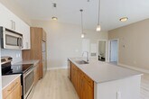This one-bedroom, one-bathroom residence in Medford, MA offers a well-designed layout across a single floor. The open-concept living area seamlessly integrates the kitchen, dining, and living spaces, creating an inviting and functional environment. The kitchen is a standout feature, anchored by a large center island with a quartz countertop, undermount sink, and pendant lighting. Warm wood cabinetry pairs with stainless steel appliances — including a refrigerator, range, microwave, and dishwasher — and light hardwood-style flooring runs throughout the main living areas. The living room is bathed in natural light from sliding glass doors that open onto a private balcony with neighborhood views. A fireplace with a clean wood mantel adds a cozy focal point to the space. The bedroom offers plush carpeting, a generously sized window, and access to two closets, including a walk-in with built-in wire shelving. The bathroom features classic white subway tile surrounding a soaking tub and shower combination, with dark tile flooring. Additional conveniences include a dedicated laundry area and a utility room, rounding out this thoughtfully appointed Medford residence.