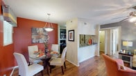 This single-floor residence showcases a thoughtfully designed interior with rich hardwood flooring flowing throughout the main living areas. The dining room makes a strong visual impression with a bold terracotta accent wall, a round glass-top dining table, white upholstered chairs, and a modern pendant light overhead. Natural light filters in through a nearby window, enhancing the warm, inviting atmosphere.

The kitchen is efficiently laid out with dark cabinetry, granite-style countertops, and a full suite of stainless steel appliances, including an electric range, over-the-range microwave, and refrigerator. A pass-through counter connects the kitchen to the adjacent living and dining spaces, promoting an open feel.

The living room is bright and comfortable, centered around a ceiling fan with lighting and sliding glass doors that open to a private balcony with outdoor seating and greenery views. A gray accent wall grounds the space with a modern touch.

The bedroom offers plush carpet, a deep slate-blue accent wall, and a generous walk-in closet. A window with striped drapery allows for natural light while maintaining privacy.

Two full bathrooms complete the layout — one featuring a tub/shower combination and granite vanity, the other with a stand-up shower and matching dark wood cabinetry — both finished with hardwood-style flooring and framed artwork.