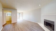This single-floor residence presents a well-organized layout with a bright, neutral aesthetic carried consistently throughout the space. The main living area is generously proportioned, featuring light wood-style laminate flooring, soft gray walls, and a textured ceiling that adds subtle character. A fireplace with a clean white mantel serves as a focal point in the living room, complemented by a sliding glass door that invites natural light and provides outdoor access. Recessed lighting and a chandelier-style fixture in the adjoining dining area contribute to a warm, layered ambiance. A secondary living or sitting area near the front entry shares the same open feel, with a full-light front door that brightens the space. The bedrooms are well-sized, each equipped with ceiling fans and windows that frame views of the surrounding greenery, ensuring both comfort and ventilation. The bathroom features a wide vanity with white cabinetry, a large mirror with overhead globe lighting, and wood-style flooring that ties the space together cohesively. Throughout the residence, consistent finishes — from the trim work to the flooring — create a unified, move-in ready environment suitable for a variety of lifestyles.