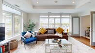 This well-appointed one-bedroom, one-bathroom residence in Saugus, MA offers a thoughtfully designed open-concept layout across a single floor. The kitchen is a standout feature, showcasing two-tone cabinetry with white upper cabinets and wood-grain lower cabinets, a white subway tile backsplash, quartz countertops, a center island with seating, and a full suite of stainless steel appliances including a gas range, built-in microwave, dishwasher, and French door refrigerator. Elegant pendant lighting accents the kitchen, which flows seamlessly into the dining and living areas. The living room is bathed in natural light through expansive floor-to-ceiling windows that frame outdoor views of the surrounding neighborhood and landscape. The dining area mirrors this brightness with its own large window. Warm hardwood flooring runs throughout the main living spaces, enhancing the modern aesthetic. The spacious primary bedroom features a tray ceiling, recessed lighting, a sliding closet, and additional windows that carry in natural light. The bathroom is finished with light wood vanity cabinetry, quartz countertops, a large mirror, and neutral tile flooring. A utility room completes the layout, adding practical functionality to this contemporary residence.