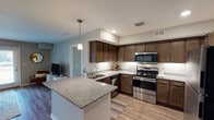 This single-floor residence offers a thoughtfully designed layout that balances functionality and comfort across its key living spaces. The kitchen serves as a standout feature, showcasing rich dark-stained cabinetry, granite countertops with under-cabinet lighting, and a full suite of stainless steel appliances including a range, microwave, dishwasher, and refrigerator. A peninsula with pendant lighting extends the workspace and provides an ideal spot for casual dining or entertaining. Light wood-style flooring flows throughout the main living areas, lending a warm, cohesive feel. The living room is bright and welcoming, with French doors that invite natural light and provide direct outdoor access. A dedicated dining area sits adjacent to the living space, creating a comfortable open-concept atmosphere. Two well-sized bedrooms feature plush carpeting and ample natural light, with one bedroom benefiting from a large window. The unit includes two bathrooms: one with a walk-in shower and another with a full tub-shower combination, both featuring granite-topped vanities, wood-tone cabinetry, and brushed nickel fixtures. Neutral wall tones and clean architectural lines throughout contribute to a calm, modern ambiance.