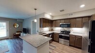 This single-floor residence offers a thoughtfully designed layout that balances functionality and comfort across its key living spaces. The kitchen serves as a standout feature, showcasing rich dark-stained cabinetry, granite countertops with under-cabinet lighting, and a full suite of stainless steel appliances including a range, microwave, dishwasher, and refrigerator. A peninsula with pendant lighting extends the workspace and provides an ideal spot for casual dining or entertaining. Light wood-style flooring flows throughout the main living areas, lending a warm, cohesive feel. The living room is bright and welcoming, with French doors that invite natural light and provide direct outdoor access. A dedicated dining area sits adjacent to the living space, creating a comfortable open-concept atmosphere. Two well-sized bedrooms feature plush carpeting and ample natural light, with one bedroom benefiting from a large window. The unit includes two bathrooms: one with a walk-in shower and another with a full tub-shower combination, both featuring granite-topped vanities, wood-tone cabinetry, and brushed nickel fixtures. Neutral wall tones and clean architectural lines throughout contribute to a calm, modern ambiance.