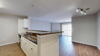 Located at 900 Crest Ln in Fort Lee, NJ, this well-appointed three-bedroom, two-bathroom residence offers a thoughtfully designed single-floor layout. The open-concept living and kitchen area serves as the heart of the home, where rich dark hardwood flooring flows seamlessly from the living room to the kitchen peninsula. The living room is anchored by a classic fireplace with a white mantel and features a sliding glass door that fills the space with natural light and provides outdoor views. The kitchen is equipped with stainless steel appliances — including a gas range, microwave, and refrigerator — complemented by dark granite countertops, white shaker-style cabinetry with brushed nickel hardware, a tile backsplash, and a breakfast bar with seating overhang. The three bedrooms feature neutral-toned carpet and clean white trim, offering comfortable, versatile spaces. The primary bedroom is generously proportioned and opens to a hallway with closet access. Both bathrooms are finished with tile flooring and brushed nickel fixtures; one includes a full tub-shower combination, while the second bath provides additional convenience. The overall aesthetic is clean and neutral, with a cohesive palette of soft grays and whites throughout.
