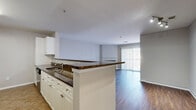 Located at 900 Crest Ln in Fort Lee, NJ, this well-appointed three-bedroom, two-bathroom residence offers a thoughtfully designed single-floor layout. The open-concept living and kitchen area serves as the heart of the home, where rich dark hardwood flooring flows seamlessly from the living room to the kitchen peninsula. The living room is anchored by a classic fireplace with a white mantel and features a sliding glass door that fills the space with natural light and provides outdoor views. The kitchen is equipped with stainless steel appliances — including a gas range, microwave, and refrigerator — complemented by dark granite countertops, white shaker-style cabinetry with brushed nickel hardware, a tile backsplash, and a breakfast bar with seating overhang. The three bedrooms feature neutral-toned carpet and clean white trim, offering comfortable, versatile spaces. The primary bedroom is generously proportioned and opens to a hallway with closet access. Both bathrooms are finished with tile flooring and brushed nickel fixtures; one includes a full tub-shower combination, while the second bath provides additional convenience. The overall aesthetic is clean and neutral, with a cohesive palette of soft grays and whites throughout.