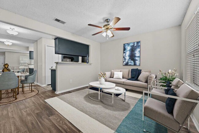 Sala de estar con sofá beige, mesa de centro blanca, ventilador de techo, cuadro enmarcado y vista abierta al comedor y la cocina. - Walnut Creek