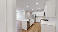 This single-floor residence at 7600 Pennsy Pky offers a thoughtfully designed layout with 2 bedrooms and 2 bathrooms. The open-concept kitchen and living area serves as the heart of the home, featuring warm hardwood-style flooring, recessed lighting, and neutral gray walls that create a bright, cohesive atmosphere. The kitchen is equipped with crisp white shaker cabinetry extending to the ceiling for ample storage, light quartz countertops, stainless steel appliances including a refrigerator and microwave, and a central island with an integrated sink — ideal for both cooking and casual dining. The living area is bathed in natural light through French doors that open to an outdoor space, enhancing the sense of openness. Both bedrooms are carpeted in a soft neutral tone and include ceiling fans and windows that invite natural light. The primary bedroom features a double-door closet for generous storage. The two bathrooms are finished in clean white with brushed nickel fixtures, each offering a full tub-shower combination. The consistent use of neutral tones, modern hardware, and quality finishes throughout gives this residence a polished, move-in-ready appeal.