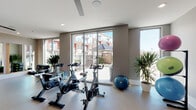 Located at 900 Hobbs Rd in Greensboro, North Carolina, this single-floor fitness and wellness facility is thoughtfully designed to support a wide range of exercise activities. The space is divided into two distinct yet connected zones, seamlessly accessible through stylish sliding barn doors.

The cycling area is bathed in natural light streaming through expansive floor-to-ceiling sliding glass doors, which open to views of the surrounding community courtyard and pool. This bright, airy section is equipped with Spinning bikes, step platforms, a plyo box, a stability ball, and lush potted plants, creating an energizing yet welcoming atmosphere. Herringbone-patterned flooring adds a refined aesthetic detail throughout.

The adjacent open studio is generously proportioned, offering ample room for yoga, stretching, dance, or group fitness classes. Dual ceiling fans provide comfortable airflow, while full-length mirrored walls visually expand the space and support form-focused workouts. Decorative silver yoga-pose sculptures adorn the walls, reinforcing the wellness-oriented character of the room. Recessed lighting ensures the studio is well-lit at all times.

Together, the two areas create a cohesive, modern fitness environment that balances functionality with contemporary design, making it a well-equipped destination for a variety of fitness pursuits.