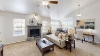 Located at 11308 SW Fifth St in Yukon, Oklahoma, this single-story home offers a well-designed open floor plan that seamlessly connects its main living areas. The living room serves as a central gathering space, highlighted by soaring vaulted ceilings, a ceiling fan, and a stylish fireplace with a gray-toned surround. Multiple windows allow natural light to fill the room, creating a bright and welcoming atmosphere. Adjacent to the living room, a dedicated area provides space for a home office or study, flowing naturally into a dining area with its own pendant lighting and generous window coverage. The kitchen features a large peninsula with a white countertop and undermount sink, white upper cabinetry, gray lower cabinetry, subway tile backsplash, and stainless steel appliances, combining function with a clean, modern aesthetic. The primary bedroom is generously proportioned with vaulted ceilings, plush carpeting, a ceiling fan, and direct access to both a walk-in closet and a private en suite bathroom. The bathroom is appointed with gray vanity cabinetry, a white countertop, a broad mirror with vanity lighting, and tile flooring. Additional bedrooms also feature high ceilings and en suite or nearby bathroom access, completing a thoughtfully laid-out home.