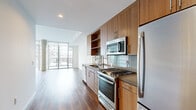 Located in San Diego's vibrant East Village neighborhood, this single-floor unit offers a well-designed layout that maximizes its compact footprint. The open-concept living and kitchen area serves as the heart of the space, featuring warm hardwood-style flooring that flows throughout. The kitchen is outfitted with rich walnut-toned cabinetry, stainless steel appliances including a gas range, microwave, and refrigerator, complemented by a tiled backsplash and a double undermount sink. Floor-to-ceiling sliding glass doors flood the living area with natural light and provide views of the surrounding cityscape, creating a bright and airy atmosphere.

The living area offers clean white walls and an open canvas for flexible furniture arrangements. A hallway connects the main living space to the private areas of the unit. Both bathrooms are finished in a clean, modern aesthetic: one features large-format tile flooring, a sleek white vanity with an LED-lit mirror, while the second includes a full soaking tub with white subway tile surround and built-in shelving. The walk-in closet provides practical storage with multiple shelving tiers and hanging rods, finished with matching hardwood-style flooring.
