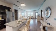 This single-floor residence offers a thoughtfully designed open-concept layout that seamlessly connects the kitchen, dining, and living areas. The kitchen is a standout feature, outfitted with dark espresso cabinetry, granite countertops, a classic white subway tile backsplash, stainless steel appliances including a gas range and French door refrigerator, and a central island with bar seating illuminated by a stylish pendant light. Rich hardwood-style flooring flows throughout the main living areas, complementing the neutral, light-filled palette. The living room is anchored by crown molding, a ceiling fan, and multiple windows fitted with horizontal blinds that invite natural light while maintaining privacy. Two bedrooms are finished with plush carpet, ceiling fans, and ample natural light from well-positioned windows. The bedrooms feature rustic wood bed frames and matching nightstands, creating a warm and cohesive aesthetic. The bathroom includes a dual-sink vanity with granite countertops, dark cabinetry mirroring the kitchen, and a large mirror that enhances the sense of space. A walk-in pantry or storage closet is also accessible from the main living area. Overall, the space presents a clean, contemporary design with cohesive finishes throughout.