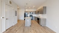 Located at 6230 Glencoe St in Commerce City, Colorado, this thoughtfully designed one-bedroom, one-bathroom residence offers a contemporary living experience on a single floor. The open-concept layout seamlessly connects the kitchen, dining, and living areas, creating a bright and cohesive space ideal for both everyday living and entertaining. The modern kitchen is a standout feature, showcasing sleek wood-toned cabinetry, a subway tile backsplash, granite countertops, a central island with pendant lighting, and a full suite of stainless steel appliances. Light hardwood-style flooring flows throughout the main living areas, adding warmth and continuity. The bedroom is a comfortable retreat, carpeted for added coziness and featuring a large window that fills the room with natural light while offering views of the surrounding neighborhood. Two closets provide generous storage, including an organized wire-shelving system for efficient use of space. The unit also includes an in-unit laundry area and a dedicated utility room for added convenience. Clean white walls, recessed lighting, and a ceiling fan in the living area contribute to the space's fresh, modern ambiance. A balcony access point visible in the floor plan further enhances the appeal of this well-appointed residence.