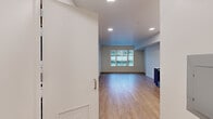 This single-floor unit presents a clean, contemporary design characterized by an open and airy layout. The main living area is finished with warm wood-look flooring and is illuminated by recessed lighting overhead, complemented by a large window dressed with vertical blinds that allows natural light to fill the space and offers views of the surrounding urban streetscape.

The kitchen is thoughtfully appointed with a two-tone cabinetry scheme, featuring light upper cabinets and darker wood-grain lower cabinets, paired with white countertops and a subway tile-style backsplash. Stainless steel appliances — including a refrigerator, range, microwave, and dishwasher — complete the functional and stylish cooking space, which flows seamlessly into the living area.

The full bathroom features a single undermount sink set into a white countertop with warm wood-toned cabinetry below, a large mirror, chrome fixtures, and a full tub-shower combination, all finished in a clean, neutral palette.

Storage is well-addressed through a generously sized walk-in closet equipped with wire shelving and hanging rods along two walls, finished with plush carpet underfoot. The overall ambiance of the unit is bright, modern, and move-in ready.