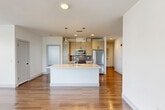 This well-appointed 2-bedroom, 2-bathroom residence in Framingham, MA offers a thoughtfully designed single-floor layout with modern finishes throughout. The heart of the home is an open-concept living, dining, and kitchen area bathed in natural light, where warm hardwood-style flooring flows seamlessly throughout. The kitchen is a standout feature, equipped with stainless steel appliances including a full-size refrigerator, range, and microwave, complemented by light wood cabinetry, a tile backsplash, and a large center island with a white countertop and undermount sink — ideal for both cooking and entertaining. The primary bedroom is a generously sized retreat featuring a wide bank of windows that frame outdoor views and allow ample natural light. The second bedroom offers plush carpeting, a window with outdoor views, and a clean, neutral palette. Both bathrooms are finished with light tile flooring and wood-toned vanity cabinetry with modern black hardware. Additional highlights include three closets for abundant storage, a dedicated laundry area with in-unit washer and dryer, a utility room, and a hallway connecting all spaces efficiently. Clean white walls, modern panel doors with matte black hardware, and consistent finishes create a cohesive, contemporary aesthetic throughout.