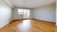 Located at 1450 First St E in Cornwall, Ontario, this well-appointed one-bedroom, one-bathroom unit offers a thoughtfully designed layout across a single floor. Warm hardwood-style flooring runs continuously throughout the space, lending a cohesive and inviting feel to every room.

The living room is generously sized and bathed in natural light from a large window that frames views of the surrounding greenery. Baseboard heating ensures year-round comfort. The bedroom offers a comfortable footprint with its own window providing additional natural light and outdoor views, making it a bright and restful retreat.

The kitchen is efficiently laid out, featuring white shaker-style cabinetry, a dual-toned countertop, a stainless steel sink, and a full-size refrigerator — providing ample storage and functionality. The bathroom is clean and well-finished, complete with a full tub and shower combo surrounded by white tile, a vanity with storage, and consistent hardwood-style flooring.

Two hallways connect the rooms, ensuring a practical flow throughout the unit. Neutral white walls throughout the space create a bright, airy ambiance that complements the warm flooring. This unit presents a clean, move-in-ready space ideal for those seeking comfortable, low-maintenance living in Cornwall.
