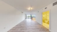 Located at 4400 West Sunrise Boulevard in Plantation, FL, this efficiently designed studio offers a clean, modern aesthetic throughout its single-floor layout. The open-plan living and kitchen area is bathed in natural light, thanks to a full-width sliding glass door that frames lush outdoor views and provides access to a private balcony. Light wood-style flooring extends throughout the space, complementing the crisp white walls and creating a bright, airy atmosphere. A geometric cage-style ceiling fixture adds a contemporary accent to the living area.

The kitchen is well-appointed with sleek white flat-front cabinetry, dark stone countertops, a full suite of stainless steel appliances including a side-by-side refrigerator with water dispenser, electric range, microwave, and dishwasher, along with a tile backsplash and track lighting overhead. The layout maximizes functionality while maintaining a clean, uncluttered look.

The bathroom features a frameless glass-enclosed walk-in shower with large-format marble-style tile, a dark stone vanity countertop, and light tile flooring, offering a polished, spa-inspired finish. The entry area includes an electrical panel and a closet, rounding out this well-organized and stylishly updated space.