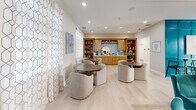 Located at 32015 Azure Ave in Rehoboth Beach, Delaware, this single-floor community clubhouse offers a thoughtfully designed gathering space with a coastal aesthetic that reflects its seaside surroundings. Light hardwood flooring runs throughout, complementing the bright, neutral palette accented by bold teal hues that evoke the nearby Atlantic waters.

The open-concept living room serves as the heart of the space, anchored by a white-painted brick fireplace flanked by built-in bookshelves filled with curated décor and books. Plush teal velvet armchairs and a ceiling fan with a shiplap-paneled ceiling overhead create a welcoming, relaxed atmosphere. Adjacent to the living area, a versatile lounge features comfortable curved seating around round tables, with sheer geometric-patterned curtains framing large windows that invite ample natural light and ocean-inspired artwork adorning the walls.

The dining and kitchen area is a standout, boasting a generous island with a quartz countertop and upholstered bar seating, warm honey-toned cabinetry, pendant lighting, and large windows overlooking the outdoors. A built-in wet bar with open shelving adds to the entertaining functionality.

The game room makes a bold statement with a dramatic floor-to-ceiling teal board-and-batten accent wall, a pool table, wall-mounted TV, and direct access to an outdoor area through glass doors, completing this dynamic and inviting communal space.