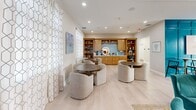 Located at 32015 Azure Ave in Rehoboth Beach, Delaware, this single-floor community clubhouse offers a thoughtfully designed gathering space with a coastal aesthetic that reflects its seaside surroundings. Light hardwood flooring runs throughout, complementing the bright, neutral palette accented by bold teal hues that evoke the nearby Atlantic waters.

The open-concept living room serves as the heart of the space, anchored by a white-painted brick fireplace flanked by built-in bookshelves filled with curated décor and books. Plush teal velvet armchairs and a ceiling fan with a shiplap-paneled ceiling overhead create a welcoming, relaxed atmosphere. Adjacent to the living area, a versatile lounge features comfortable curved seating around round tables, with sheer geometric-patterned curtains framing large windows that invite ample natural light and ocean-inspired artwork adorning the walls.

The dining and kitchen area is a standout, boasting a generous island with a quartz countertop and upholstered bar seating, warm honey-toned cabinetry, pendant lighting, and large windows overlooking the outdoors. A built-in wet bar with open shelving adds to the entertaining functionality.

The game room makes a bold statement with a dramatic floor-to-ceiling teal board-and-batten accent wall, a pool table, wall-mounted TV, and direct access to an outdoor area through glass doors, completing this dynamic and inviting communal space.