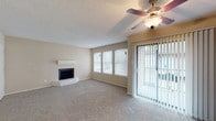 This single-floor residence offers a well-organized layout with a comfortable, neutral palette throughout. The living room serves as the central gathering space, highlighted by a brick-surround fireplace with a white mantel, soft carpeting, a ceiling fan with integrated lighting, and a sliding glass door that opens to an outdoor area, allowing natural light to flow freely into the room. Multiple windows further enhance the bright, airy atmosphere.

The kitchen features white cabinetry with gold-tone hardware, speckled countertops, and a double stainless steel sink. A pass-through window connects the kitchen directly to the living area, maintaining an open, communicative feel between the two spaces.

The bedroom is generously sized with plush carpeting, neutral walls, a textured ceiling, and a window for natural light. It is served by a spacious walk-in closet outfitted with multiple shelving rods along the walls, offering substantial storage capacity.

Two bathrooms are present in the unit. One features a tub-shower combination with white tile surround and wood-look flooring. The other includes a vanity with speckled countertops, a mirror, and a compartmentalized toilet area, also finished with wood-look flooring. Textured ceilings are consistent throughout the space.