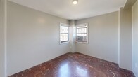 Located at 1230 Pendleton St, Unit 7A in Columbia, South Carolina, this two-bedroom, one-bathroom residence offers a compact and efficiently arranged floor plan across a single level. The unit is characterized by rich, dark parquet hardwood flooring that runs throughout both bedrooms and the connecting hallway, lending a classic warmth to the interior.

The primary bedroom is the larger of the two rooms and features two windows fitted with window A/C units, allowing for natural light and views of the surrounding neighborhood. The second bedroom similarly benefits from a window with its own A/C unit, keeping the space comfortable year-round. Both rooms are finished with neutral, light gray walls that complement the dark flooring.

A connecting hallway leads between the bedrooms and includes access to a dedicated closet, providing practical storage within the unit. White two-panel interior doors with brass hardware are consistent throughout, contributing to a cohesive, traditional aesthetic.

The bathroom features classic black-and-white basketweave tile flooring and white square wall tile surrounding a full soaking tub with an overhead shower. A toilet and wall-mounted towel bar complete the functional layout of the bathroom.

Overall, the unit presents a straightforward, traditional design with durable finishes and practical amenities in a central Columbia location.
