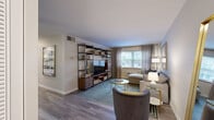 This two-bedroom, one-bathroom apartment at 500 Fulton St E in Grand Rapids, Michigan, offers a well-organized single-floor layout that makes efficient use of its space. The inviting living room features hardwood-style flooring, a large window that draws in natural light, and ample room for comfortable seating arrangements. An open shelving unit provides both display and storage options, contributing to the room's modern, functional aesthetic. The dedicated dining area adjoins the living space and includes a ceiling fan, with a framed mirror accent on the wall adding depth to the room. The kitchen is equipped with white cabinetry, dark countertops, a stainless steel sink with a brushed nickel faucet, and a stainless steel refrigerator — offering a clean, practical workspace. Both bedrooms are carpeted and feature windows with curtains, providing a cozy and restful atmosphere. The primary bedroom offers generous space, while the second bedroom is well-proportioned and equally comfortable. The bathroom is finished with classic white tile, a shower-tub combination, and framed wall art, delivering a clean and timeless look. Throughout the unit, neutral tones and consistent finishes create a cohesive and welcoming ambiance.