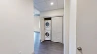 Located at 330 Main St in downtown Utica, NY, this thoughtfully designed one-bedroom, one-bathroom unit blends industrial character with modern finishes. The open-concept layout is anchored by durable hardwood-style flooring throughout and soaring ceilings with exposed ductwork, lending a distinct loft aesthetic to the living spaces.

The well-appointed kitchen features crisp white shaker cabinetry, light granite-style countertops, a subway tile backsplash, and a full suite of stainless steel appliances including a refrigerator, range, microwave, and dishwasher. Oversized industrial-style windows frame views of the surrounding downtown streetscape, flooding the kitchen and living areas with abundant natural light.

The spacious bedroom offers a generous footprint, large windows with city views, and access to two closets — including a walk-in closet outfitted with built-in shelving and hanging rods for ample storage. The bathroom is finished with light tile flooring, a glass-enclosed tub and shower combo, and a window for natural ventilation.

A dedicated in-unit laundry closet houses a stacked washer and dryer, adding everyday convenience. The unit's drop-panel ceilings in the utility areas complement the mixed architectural character of this urban residence. Baseboard heating runs throughout, ensuring comfort year-round.