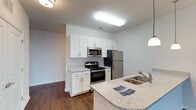 The Liberty floor plan is a well-appointed 2-bedroom, 2-bathroom residence spread across a single level, offering a generous and functional layout. The kitchen serves as a focal point of the home, featuring crisp white shaker-style cabinetry that extends to the ceiling for ample storage. Stainless steel appliances, including a gas range, built-in microwave, and refrigerator, complement the space with a sleek, modern aesthetic. The granite-look countertops add an elegant touch, while the kitchen island with a double undermount sink and pendant lighting overhead creates an ideal space for meal preparation and casual dining. Rich, dark hardwood-style flooring anchors the kitchen and flows into the surrounding living areas, providing a warm contrast to the bright white cabinetry and light-toned walls. The open-concept design connects the kitchen seamlessly to the main living area, enhancing the sense of spaciousness throughout. Recessed and flush-mount lighting ensures the space is well-lit. The overall ambiance is clean, contemporary, and move-in ready, with thoughtful details that balance style and practicality throughout the home.