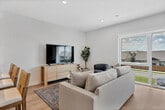 Located at 1810 N 25th Ave in Bozeman, Montana, this contemporary three-floor home offers a thoughtfully designed layout across three well-appointed levels. The ground floor houses a garage with a clean concrete floor and integrated electrical panel, providing practical storage and parking. The main living level features a bright, open-concept kitchen and living room filled with natural light from oversized windows. The kitchen is equipped with flat-front light wood cabinetry, quartz countertops, a large island with bar seating, stainless steel appliances, and a gas range. The adjacent living area offers expansive street-facing views through floor-to-ceiling windows, creating an airy, connected feel. The upper floor hosts three bedrooms, including a generously sized primary suite with direct balcony access, two additional bedrooms with large windows, a dedicated office space, and two full bathrooms. The bathrooms feature large-format tile flooring, floating wood vanities with white countertops, and glass-enclosed walk-in showers. A standout feature is the rooftop balcony, finished with wood decking and offering panoramic views of the surrounding Bozeman skyline and distant mountains. Light wood flooring, recessed lighting, and a clean neutral palette unify the home's modern aesthetic throughout.