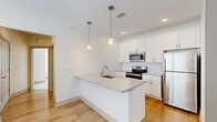 Located at 6386 Transit Rd in Depew, NY, this well-appointed 2-bedroom, 2-bathroom unit offers a thoughtfully designed single-floor layout. The open-concept kitchen and living area serves as the heart of the home, featuring crisp white shaker cabinetry, a white subway tile backsplash, granite countertops, and a full suite of stainless steel appliances including a refrigerator, range, and over-the-range microwave. A central island with a built-in sink and pendant lighting overhead adds both functionality and style. Light-toned hardwood flooring flows throughout the main living areas, enhancing the bright, airy feel of the space. The living room is generously proportioned, with a ceiling fan, recessed lighting, and multiple windows that allow ample natural light. Both bedrooms are carpeted for comfort, with the primary bedroom offering a spacious walk-in closet equipped with wire shelving. The bathrooms are finished with white cabinetry, granite countertops, and a tub-shower combination. Neutral wall tones and clean modern finishes throughout give the space a fresh, move-in-ready feel. Two hallways connect the layout efficiently, completing this functional and stylish home.