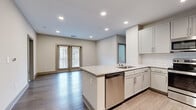 Located at 6885 Jimmy Carter Blvd in Norcross, Georgia, this single-floor residence offers a thoughtfully designed open-concept layout finished with contemporary materials throughout. The kitchen serves as a central hub of the living space, showcasing white shaker-style cabinetry, granite countertops, a subway tile backsplash, and a peninsula island with an undermount sink and stainless steel dishwasher. Stainless steel appliances, including a range and over-the-range microwave, complete the well-equipped kitchen. Light wood-tone flooring extends through the main living and kitchen areas, creating a warm, cohesive feel, while recessed lighting provides ample illumination throughout. The open living area benefits from natural light streaming through double doors fitted with blinds. Bedrooms are carpeted for comfort, with one featuring a sliding double-panel closet and another with a window offering exterior views. The space includes two bathrooms: one with a single-sink vanity topped with granite and a large framed mirror, and a primary bathroom featuring a generous double-sink granite vanity with white cabinetry and brushed nickel hardware. Neutral wall tones and clean finishes give the entire space a move-in-ready, modern aesthetic.