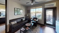 This single-floor unit offers a functional and thoughtfully designed layout that maximizes both comfort and practicality. The galley-style kitchen is outfitted with dark espresso cabinetry, stainless steel appliances including a refrigerator, microwave, and electric range, and a double sink. It opens to a peninsula breakfast bar with pendant lighting and seating, creating a natural transition into the living area. The living room is warm and inviting, featuring rich hardwood-style flooring, a ceiling fan, and large windows that frame outdoor views of the surrounding cityscape and distant hills, filling the space with abundant natural light. A sliding door provides direct access to a private balcony. The bedroom is generously sized with plush carpeting, dual large windows that capture sweeping views of the city and mountains, and a dedicated workspace area. An adjacent walk-in closet offers ample storage with built-in shelving and hanging space. The full bathroom includes a tub-shower combination and hardwood-style flooring. Throughout the unit, neutral wall tones and consistent dark-trimmed accents create a cohesive, modern aesthetic that feels both stylish and livable.