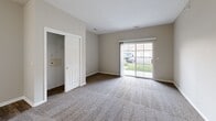 This single-story space is designed with a practical, open layout that connects key living areas seamlessly. The kitchen is a functional highlight, featuring light cream cabinetry with ample storage, a full suite of stainless steel appliances including a refrigerator, range, microwave, and dishwasher, and a peninsula counter that provides additional workspace. Wood-look plank flooring runs throughout the kitchen and connecting areas, lending a clean, cohesive aesthetic.

The living areas are generously sized, finished with neutral-toned carpet and painted in soft gray and beige tones throughout. Sliding glass doors in multiple rooms offer views of the outdoors and allow natural light to fill the space. A recessed alcove in the main living area adds an architectural detail and potential for flexible use.

The bedrooms are carpeted and include ceiling fans with light fixtures, windows with blinds for natural light and privacy, and access to closet space. The bathroom features wood-look flooring, a tub-shower combination, a vanity with under-sink storage, and a well-lit mirror above. Louvered bifold doors provide stylish separation between the bathroom and laundry area. White trim and baseboards throughout add a crisp, finished look to the overall interior.
