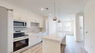 This thoughtfully designed one-bedroom, one-bathroom residence offers a bright and contemporary living experience across a single floor. The open-concept kitchen and living area serves as the heart of the home, anchored by a substantial white quartz island with pendant globe lighting overhead. The kitchen is outfitted with crisp white cabinetry, a neutral tile backsplash, stainless steel appliances including a French door refrigerator, range, microwave, and dishwasher, along with a deep undermount sink. Light wood-tone flooring flows seamlessly throughout the space, complementing the clean white walls and recessed lighting that keep the interior feeling airy and open. Large windows in the living area invite abundant natural light and views of surrounding greenery. The bedroom is a calm retreat, featuring dual windows with slatted blinds, a ceiling fan, and the same warm hardwood-style flooring. Two closets provide ample storage. The bathroom is elegantly appointed with a frameless glass walk-in shower clad in marble-look tile, a floating vanity with white countertops, and wood-toned cabinetry. A dedicated laundry area adds everyday convenience, rounding out this well-appointed and efficiently designed residence.