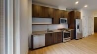 Located at Eastside Drive in Ashburn, Virginia, this single-floor residence showcases a clean, modern design throughout. Light wood flooring flows continuously across the living areas, complementing the neutral white walls and recessed lighting that create a bright, welcoming atmosphere.

The kitchen is a standout feature, outfitted with rich dark wood cabinetry extending to the ceiling for ample storage. Stainless steel appliances include a gas range, built-in microwave, dishwasher, and a side-by-side refrigerator with a water and ice dispenser. A subway tile backsplash and smooth countertops complete the contemporary aesthetic.

The living area benefits from a large sliding glass door that opens onto a private balcony, filling the space with natural light and providing views of the surrounding building exterior. The bedroom offers a generously sized, open layout with the same warm wood flooring and clean white walls.

The bathroom is finished with large-format tile on both the floor and tub surround, lending a spa-like quality to the space. A soaking tub with a curved shower curtain rod, dual under-mount sinks set into wood cabinetry with a taupe countertop, and a broad mirror round out the well-appointed bath.