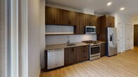 Located at Eastside Drive in Ashburn, Virginia, this single-floor residence showcases a clean, modern design throughout. Light wood flooring flows continuously across the living areas, complementing the neutral white walls and recessed lighting that create a bright, welcoming atmosphere.

The kitchen is a standout feature, outfitted with rich dark wood cabinetry extending to the ceiling for ample storage. Stainless steel appliances include a gas range, built-in microwave, dishwasher, and a side-by-side refrigerator with a water and ice dispenser. A subway tile backsplash and smooth countertops complete the contemporary aesthetic.

The living area benefits from a large sliding glass door that opens onto a private balcony, filling the space with natural light and providing views of the surrounding building exterior. The bedroom offers a generously sized, open layout with the same warm wood flooring and clean white walls.

The bathroom is finished with large-format tile on both the floor and tub surround, lending a spa-like quality to the space. A soaking tub with a curved shower curtain rod, dual under-mount sinks set into wood cabinetry with a taupe countertop, and a broad mirror round out the well-appointed bath.