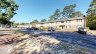 Located at 12012 Middleground Rd in Savannah, Georgia, this single-story residential complex offers a straightforward and functional layout set within a well-established, tree-lined environment. The exterior showcases classic brick and neutral-toned siding construction, lending the property a timeless and durable aesthetic. Multiple individual unit entrances are accessible directly from the parking area, providing convenient ground-level access for residents.

The property is flanked by mature pine trees that provide natural shade and a sense of privacy, contributing to a peaceful, wooded atmosphere. A generously sized asphalt parking lot runs along the front of the building, offering plentiful spaces for residents and visitors. The low-profile, single-floor design ensures ease of access throughout the entire complex.

Shuttered windows line the facade, adding a traditional architectural detail while also offering residents the ability to control natural light. The well-maintained landscaping, including neatly trimmed shrubs along the building's base, reflects consistent upkeep of the grounds. Situated in the 31419 zip code of Savannah, the property benefits from a suburban setting while remaining connected to the broader amenities of the Savannah metropolitan area.