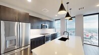 Located in the heart of downtown Columbus, this thoughtfully designed three-bedroom, four-bathroom residence offers a refined urban living experience. Wide-plank hardwood flooring flows throughout the open-concept living and kitchen areas, anchored by a striking gourmet kitchen. Dark cabinetry with gold hardware contrasts elegantly against bright quartz countertops, while a large center island with an undermount sink and dramatic pendant lighting serves as the kitchen's focal point. Stainless steel appliances complete the chef-ready space. Floor-to-ceiling windows flood the living area with natural light and frame sweeping panoramic views of the Columbus skyline. The generously sized primary bedroom features plush carpeting, a ceiling fan, and its own floor-to-ceiling window with city views, accompanied by a dedicated walk-in closet with built-in wire shelving. Additional bedrooms are well-proportioned with soft carpeting and ceiling fans. The four bathrooms are finished with large-format marble-style tile, featuring both soaking tub and walk-in shower configurations with matte black fixtures and framed mirrors. Two closets provide ample storage throughout the residence. The neutral, contemporary palette and clean architectural lines create a polished, move-in-ready environment in one of Columbus's most vibrant downtown locations.