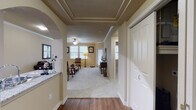 This single-floor residence offers a thoughtfully designed layout that balances comfort and style throughout. The entryway greets visitors with rich hardwood-style flooring and a striking tray ceiling with detailed crown molding, framed by a decorative archway that leads into the main living areas. The living room is generously proportioned, featuring plush carpeting, crown molding, a ceiling fan, and multiple windows that allow ample natural light to fill the space with a warm, inviting ambiance. The kitchen is a standout area, equipped with dark espresso cabinetry, granite countertops, stainless steel appliances, and a peninsula with a double sink that opens through an arched pass-through, maintaining a connected feel with the adjacent spaces. Hardwood-style flooring continues throughout the kitchen and entry areas, adding warmth and visual continuity. The bedroom is a comfortable retreat, carpeted and well-lit by windows with blinds, and is served by a dedicated bathroom featuring dark wood vanity cabinetry, granite countertops, and hardwood-style flooring. A walk-in closet adds practical storage. Throughout the residence, neutral wall tones, consistent trim work, and ceiling fans contribute to a cohesive and comfortable living environment.